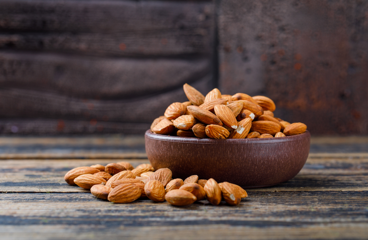 Peeled almonds in a clay plate on stone tile and wooden background, side view.